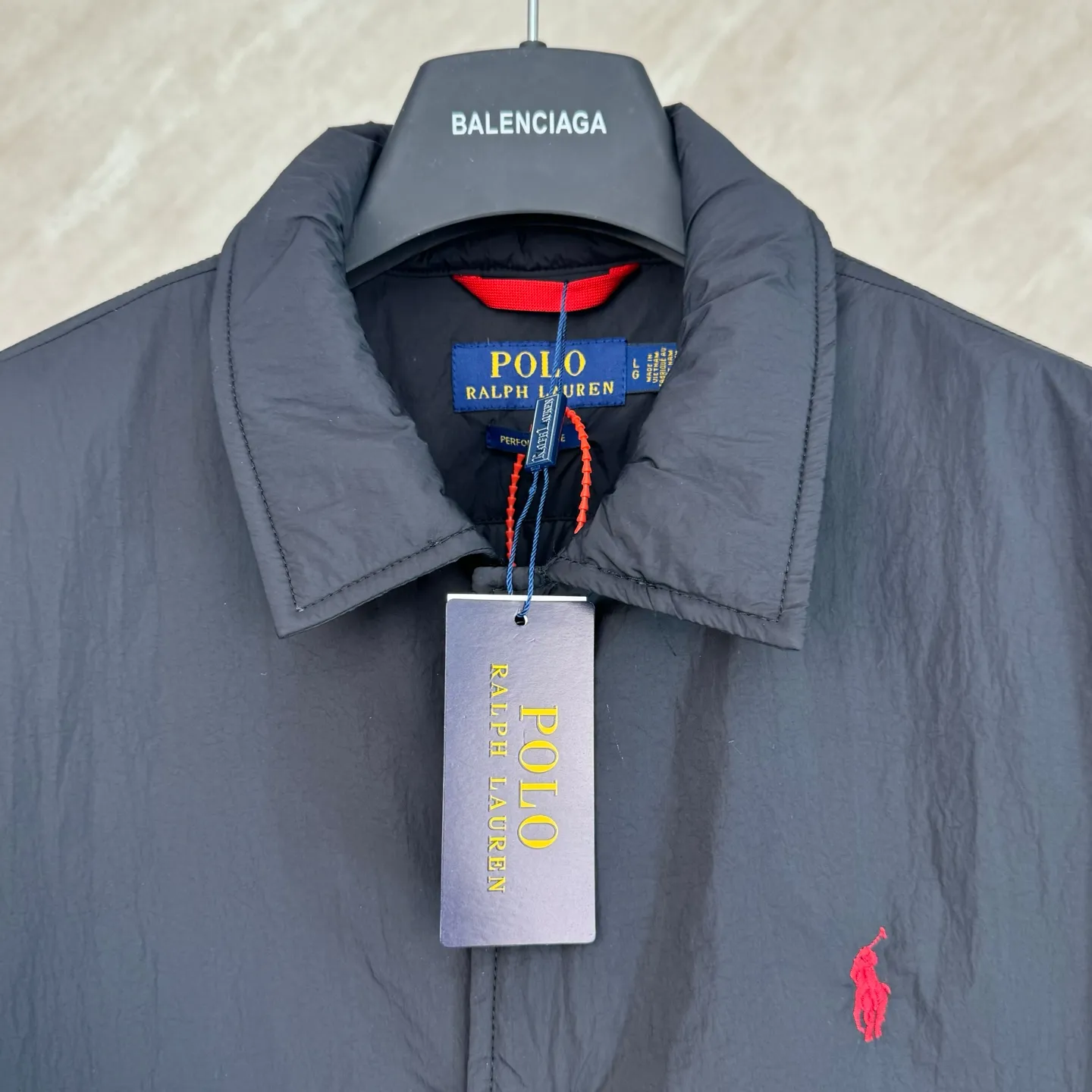 P670 25FW Ralph Lauren red label light cotton jacket (coach jacket) size s m l xl Fabric procurement: a combination of pragmatism and classic texture Material: high-density nylon taffeta Features: density is about 210T-300T, smooth and slightly matte surface, excellent windproof and waterproof performance (with DWR water-repellent treatment), strong wrinkle resistance and easy care, in line with the positioning of American casual "durable and practical".  Color: Classic dark black, using vat dyeing process (dye penetrates into the fiber), the color fastness reaches ISO level 4 or above to avoid fading or color transfer after washing.  2. Lining fabric Material: Lightweight cotton-polyester blended lining (65% Polyester + 35% Cotton) Function: Reduce friction between the fabric and inner clothing, improve wearing smoothness; blended material has both breathability and durability to avoid the stuffy feeling of pure nylon lining.  Version and cutting process Version: Classic Coach Jacket, loose version, slightly dropped shoulder line (shoulder width is 1-2cm wider than the standard version), length to the hips, and slightly tapered straight sleeves, taking into account both freedom of movement and casual style.  Embroidery technology: Polo horse logo on the left chest: flat satin stitch embroidery (satin embroidery), embroidery thread: 100% polyester high color fastness embroidery thread (the color number is consistent with the brand’s standard red color card), stitch density 12-15 stitches/cm, the outline of the horse logo is clear, and the details of the rider and horse are burr-free.  Embroidery positioning: precise positioning through the template (12cm from the neckline and 8cm from the placket) to ensure left and right symmetry and centering.  Topstitching technology: The seams of the body are made of double-needle flat seams (needle pitch 3cm/10 needles), the stitches are smooth and straight, the stitching color is dark black (the same color as the fabric), and the stitch width is 0.5cm, which enhances firmness while forming simple decorative lines.  1. Main body splicing, splicing of the front placket and body: The placket is made of double-layer folding + flat seam splicing, with a thickness of about 0.3cm to ensure that the buttons are not easily deformed when fixed; the edges of the placket are cut with a hot knife to avoid burrs.  Sleeve panels are spliced ​​to the body: the armholes are spliced ​​with round-head keyhole machine seams + flat seams. After splicing, the armholes have a natural curvature and no sense of tightness during movement; the height of the sleeves is about 8-10cm, which is in line with the loose characteristics of casual jackets.  Main button: black urea resin button, matte surface treatment, buttonholes are hand-made keyholes (6 strands of cotton thread, keyhole density 8 stitches/mm), the edges of the eyelets are smooth and without burrs.  Collar buttons: The first button on the collar is a hidden button (diameter 12mm), which prevents the collar from opening and improves the neatness of wearing.